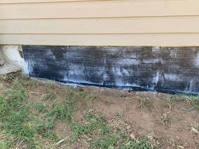 Carbon fiber reinforced polymer fabric bonded to the base of an exterior building wall.