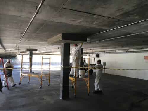Crew in coveralls preparing and strengthening a concrete column in a parking structure.